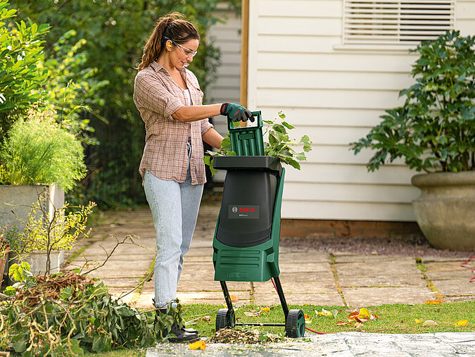 Frau zerkleinert Schnittgut nach dem Gehölzschnitt mit einem Gartenhäcksler.