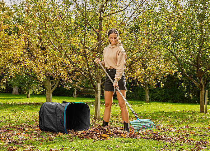 Im naturnahen Garten wird Herbstlaub mit dem Rechen gesammelt und in einem Gartensack zusammengetragen.