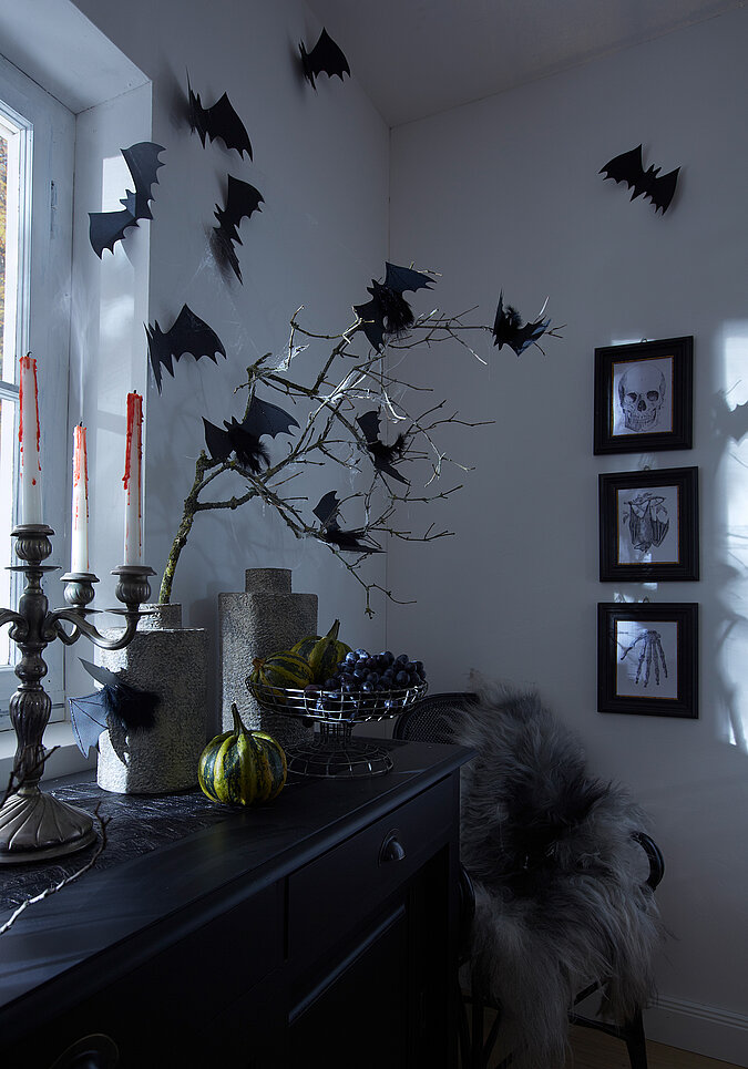 Halloween Deko selber machen: Dunkler Wohnbereich mit schwarzen Fledermäusen, Spinnweben und Ästen als gruselige Halloween-Dekoration.