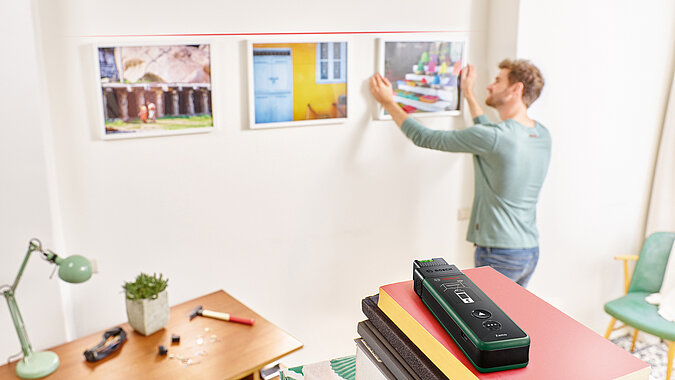 Mit einem 2-1 Entfernungsmesser überprüft ein mann, ob die Bilder an der wand gerade hängen