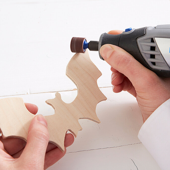 Halloween Deko selber machen: Die ausgesägte Holz-Fledermaus wird an den Kanten mit einem Schleifaufsatz geglättet.