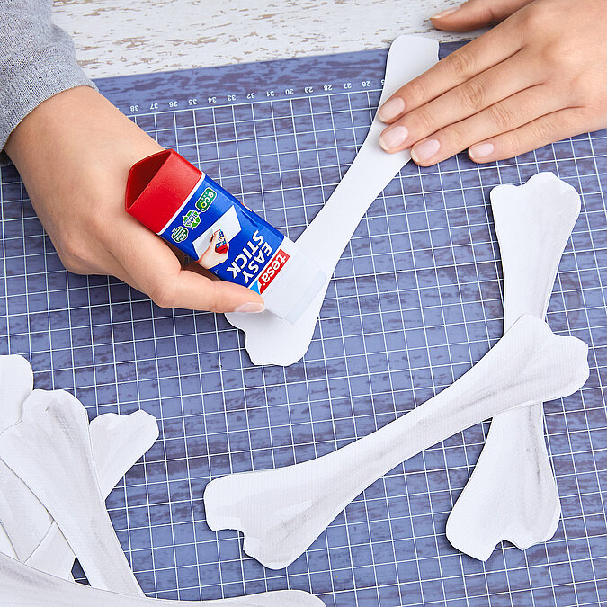 Halloween Deko selber machen: Ausgeschnittene Papierknochen werden mit Kleber zusammengesetzt und für die Deko fixiert.