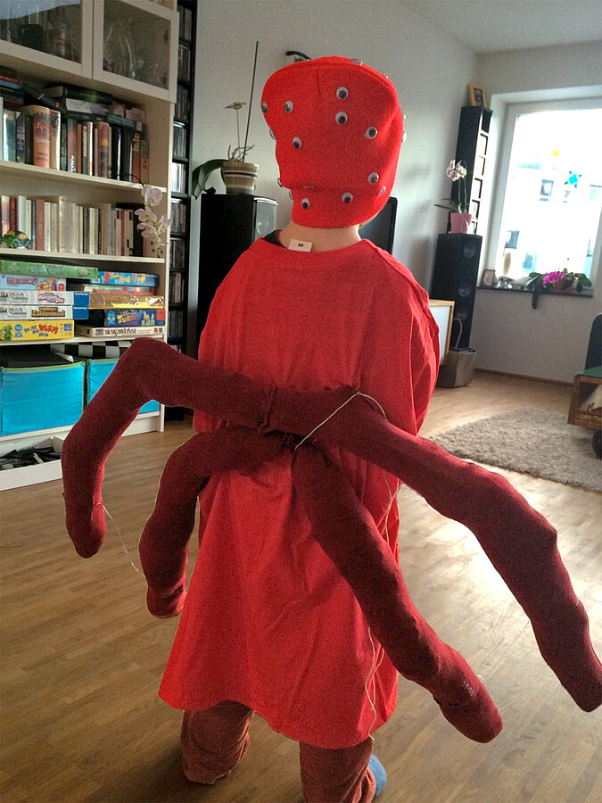 Rückansicht eines selbst gemachten Spinnen-Kostüms mit sechs zusätzlichen, beweglichen Beinen aus rotem Stoff.