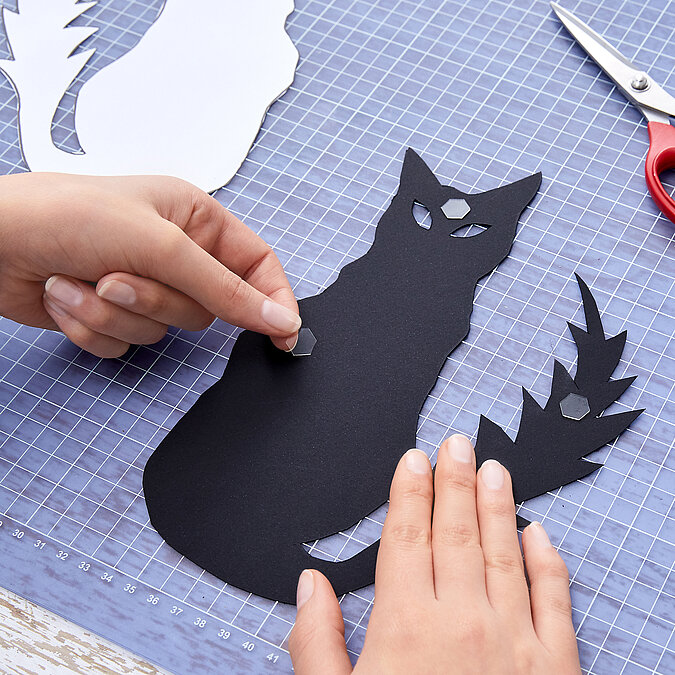 Halloween Deko selber machen: Schwarze Katzen- und Fledermausmotive werden aus Papier ausgeschnitten.