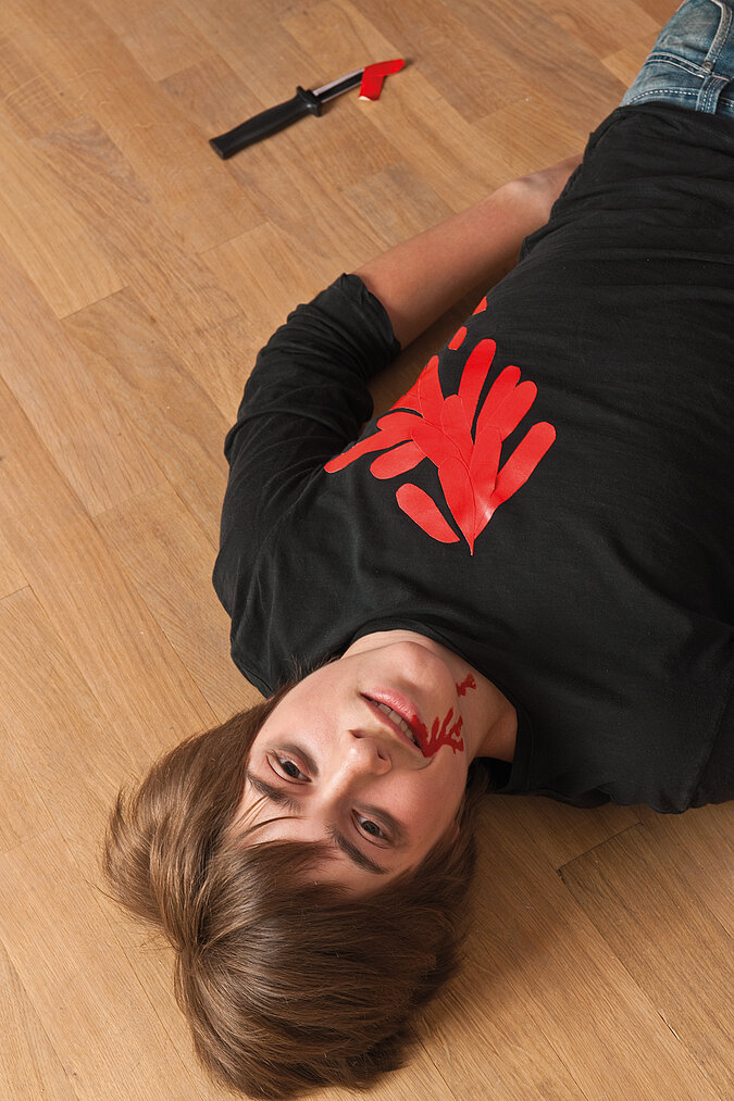 Junge im selbst gemachten Halloween-Kostüm als Mordopfer mit rotem Handabdruck auf der Brust und künstlichen Blutspuren im Gesicht.