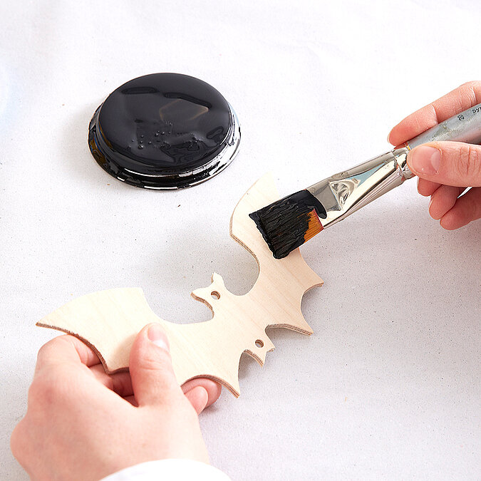 Halloween Deko selber machen: Eine ausgesägte Fledermaus aus Holz wird mit schwarzer Farbe bemalt.
