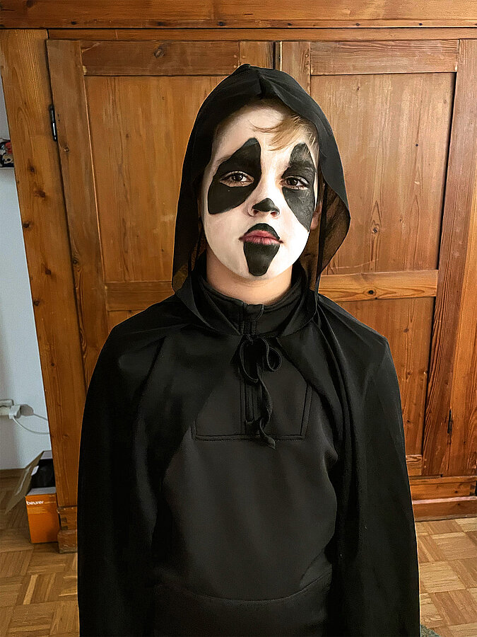 Nahaufnahme eines selbst gemachten Sensenmann-Kostüms mit schwarzer Kapuze und weiß-schwarzer Gesichtsbemalung für Halloween.