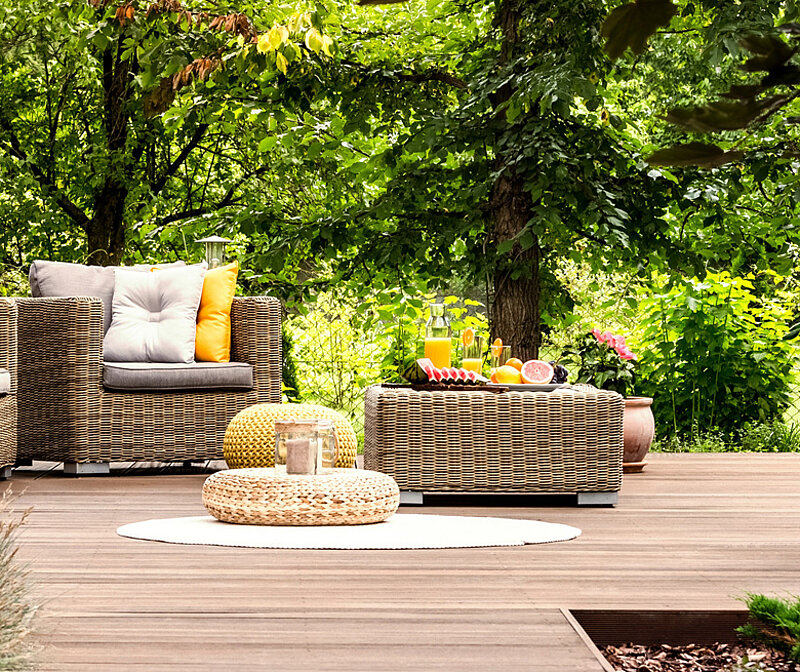 Moderne Holzterrasse mit Korbmöbeln vor in üppig grünem Garten