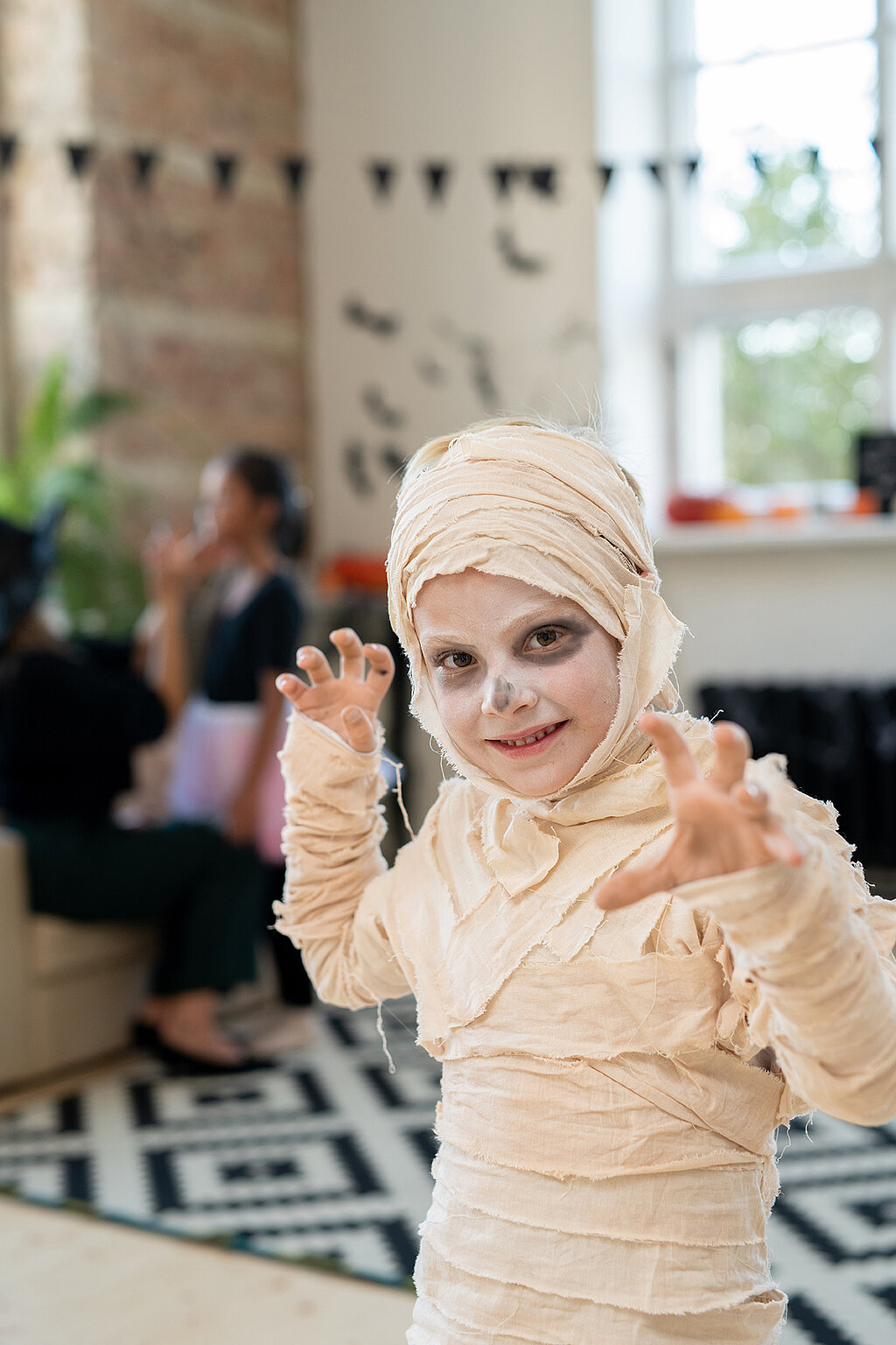  Mumien-Kostüm selber machen: Kind mit bandagiertem Kostüm und weiß geschminktem Gesicht posiert mit ausgestreckten Händen.