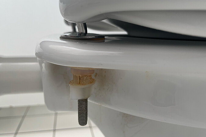 Klodeckel wechseln & pflegen – Unterseite der Toilettenbefestigung mit Schraube und Kunststoffhalterung