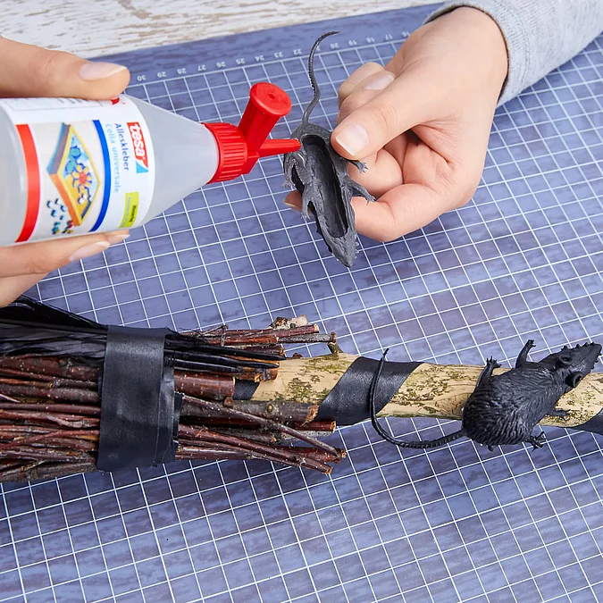 Schwarze Federn werden auf den selbst gebastelten Hexenbesen geklebt und sorgen für eine gruselige Optik.