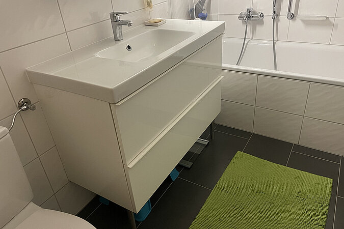 Badezimmer mit großen weissen Kacheln, Waschbecken mit Unterschrank und Badewanne