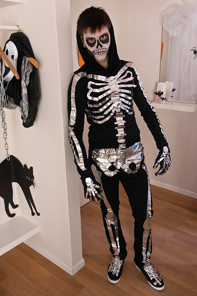 Halloween-Kostüm selber machen: Junge mit schwarz-weiß geschminktem Gesicht und selbst gebasteltem Skelett-Kostüm.