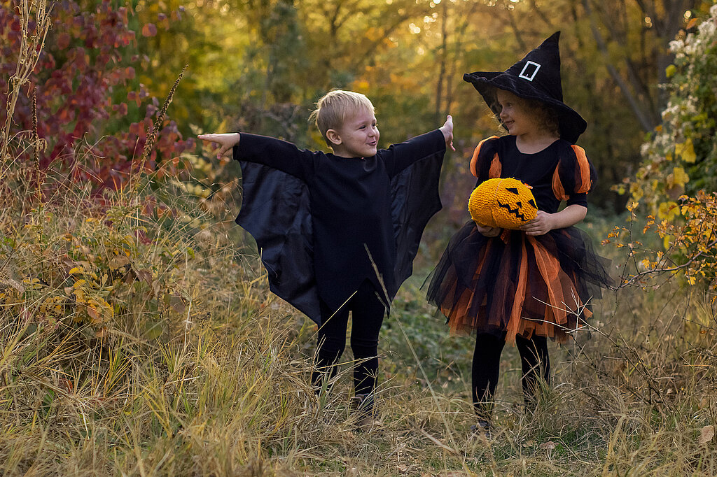 Fledermaus-Kostüm selber machen: Kind mit schwarzen Fledermausflügeln neben einer kleinen Hexe mit Hexenhut und Kürbis im herbstlichen Garten.