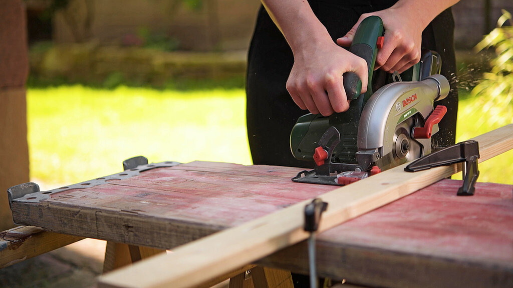 DIY-Bett aus Gerüstbohlen beim Zuschneiden einer Holzlatte mit der Handkreissäge