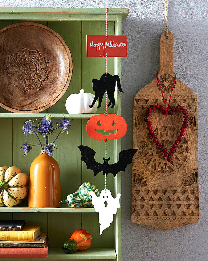Halloween Deko selber machen: Herbstlich dekorierter Eingangsbereich mit Kürbissen, Gespenstern und einer schwarzen Fledermaus auf einem Holzschild.