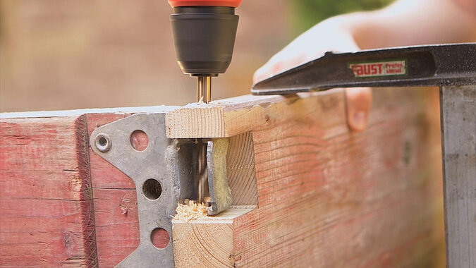 DIY-Bett aus Gerüstbohlen beim Bohren einer Aussparung für den Metallwinkel mit einem Forstnerbohrer