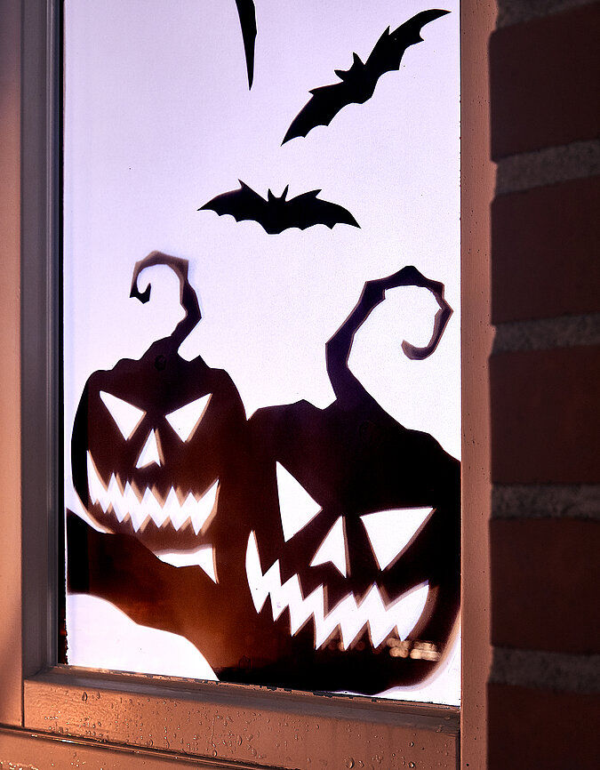 Halloween Deko selber machen: Fensterbild mit gruseligen Kürbisfratzen und Fledermaus als Halloween-Dekoration.