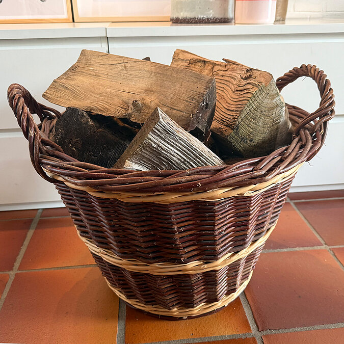Ein geflochtener Korb ist mit trockenem Brennholz für den Kamin gefüllt.