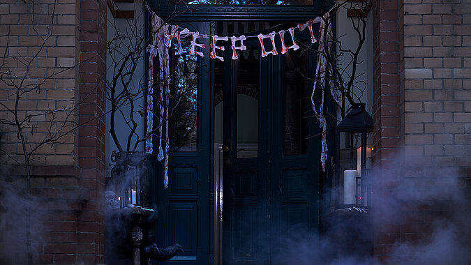 Halloween Deko selber machen: Dunkle Haustür mit gruseliger Knochen-Girlande, Spinnweben und Nebel im Halloween-Look.