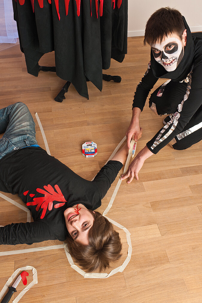 Zwei Kinder inszenieren eine gruselige Halloween-Szene mit einem selbst gebastelten Mordopfer-Kostüm und künstlichen Blutspuren.
