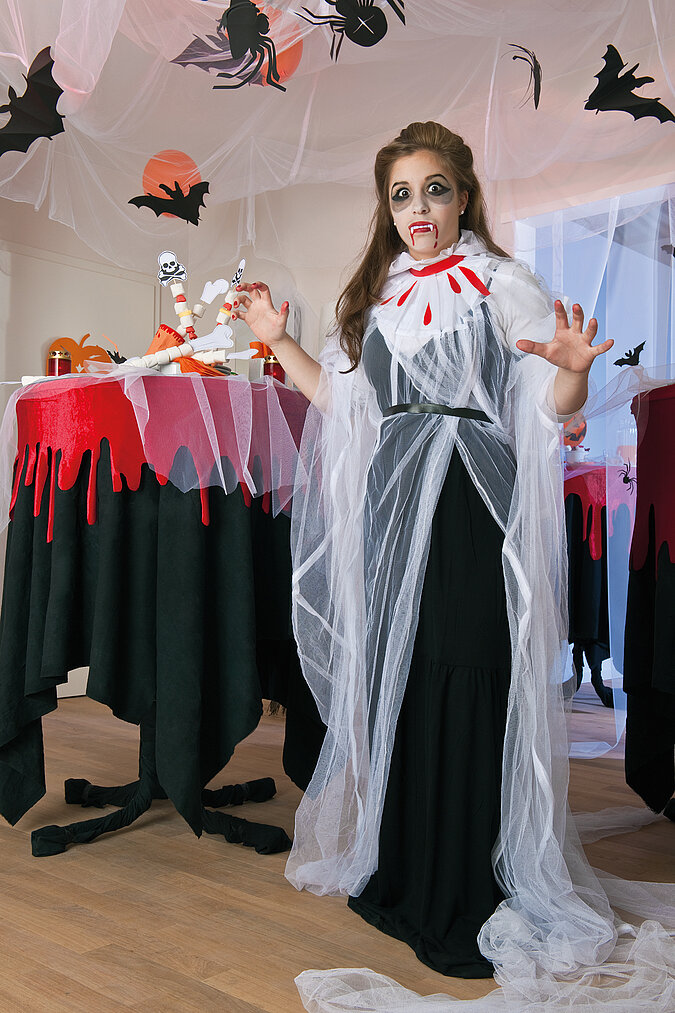 Vampir-Kostüm selber machen: Mädchen mit weißem Umhang, weißem Kragen und roten Blutspuren feiert Halloween.