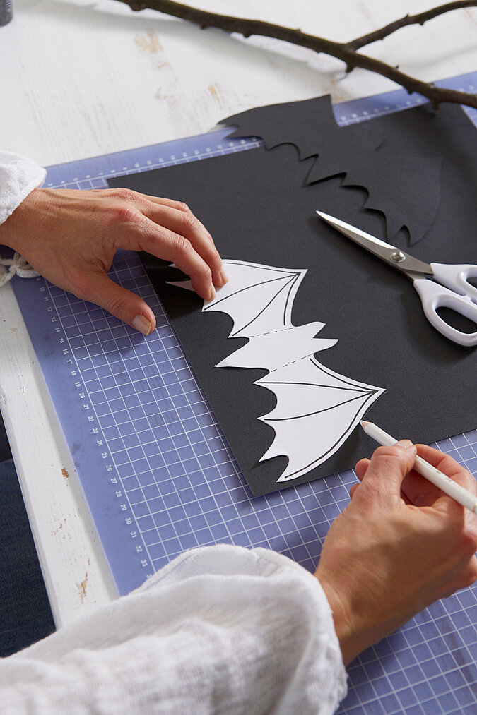 Halloween Deko selber machen: Eine Fledermaus-Vorlage wird auf schwarzes Papier übertragen und für die Halloween-Dekoration ausgeschnitten.