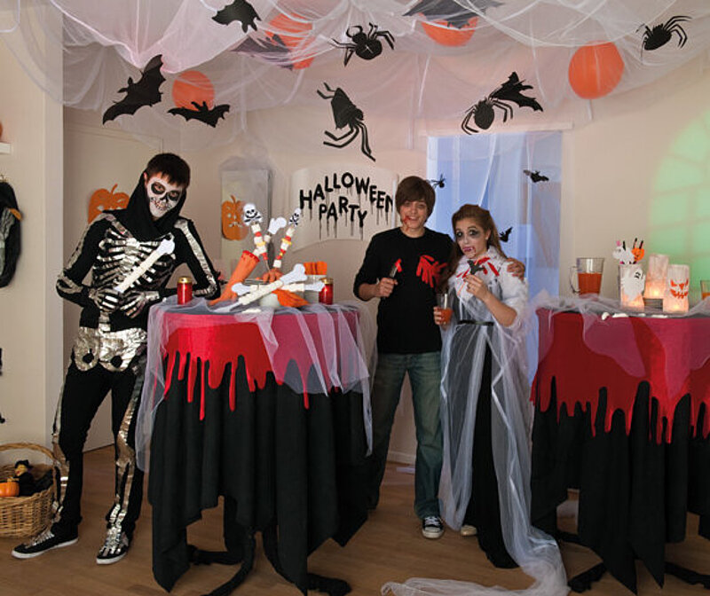 Halloween Deko selber machen: Gruselig dekorierter Partyraum mit Fledermäusen, Spinnweben, Kürbissen und Skelett.