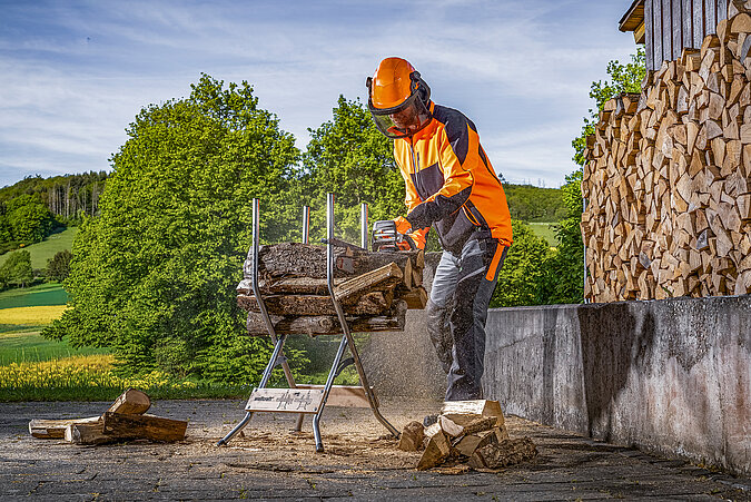 Eine Person sägt Holzstücke auf einem Sägebock auf die passende Länge für Brennholz.