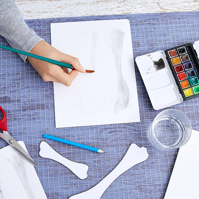 Halloween Deko selber machen: Knochenvorlage wird auf weißes Papier übertragen und für eine Halloween-Girlande vorbereitet.