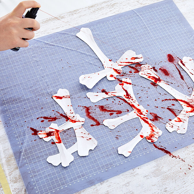 Halloween Deko selber machen: Papierknochen werden mit roter Farbe verziert und erhalten eine schaurige Halloween-Optik.